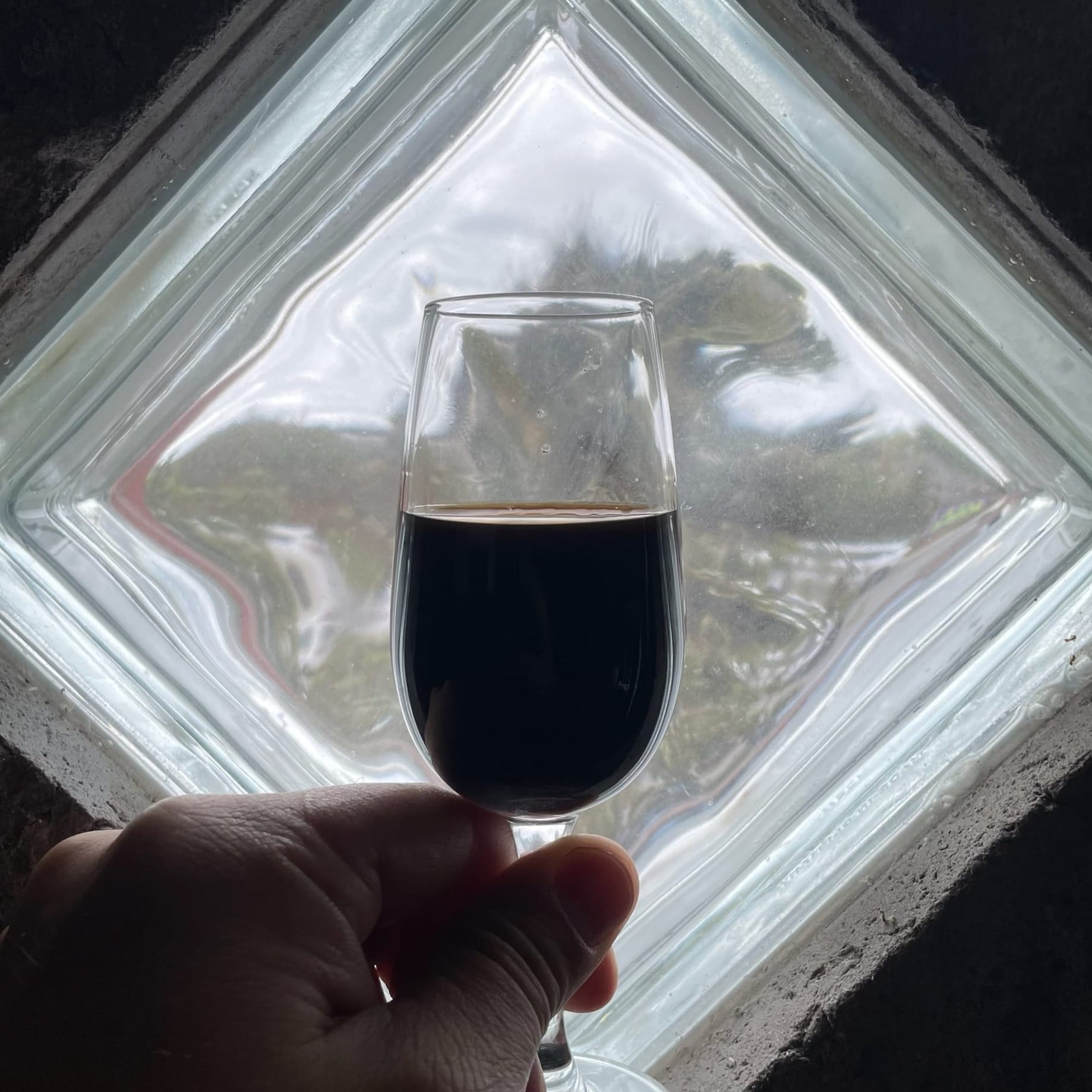 A sherry copita partly full of opaque, black liquid held in front of a diagonal glass window.