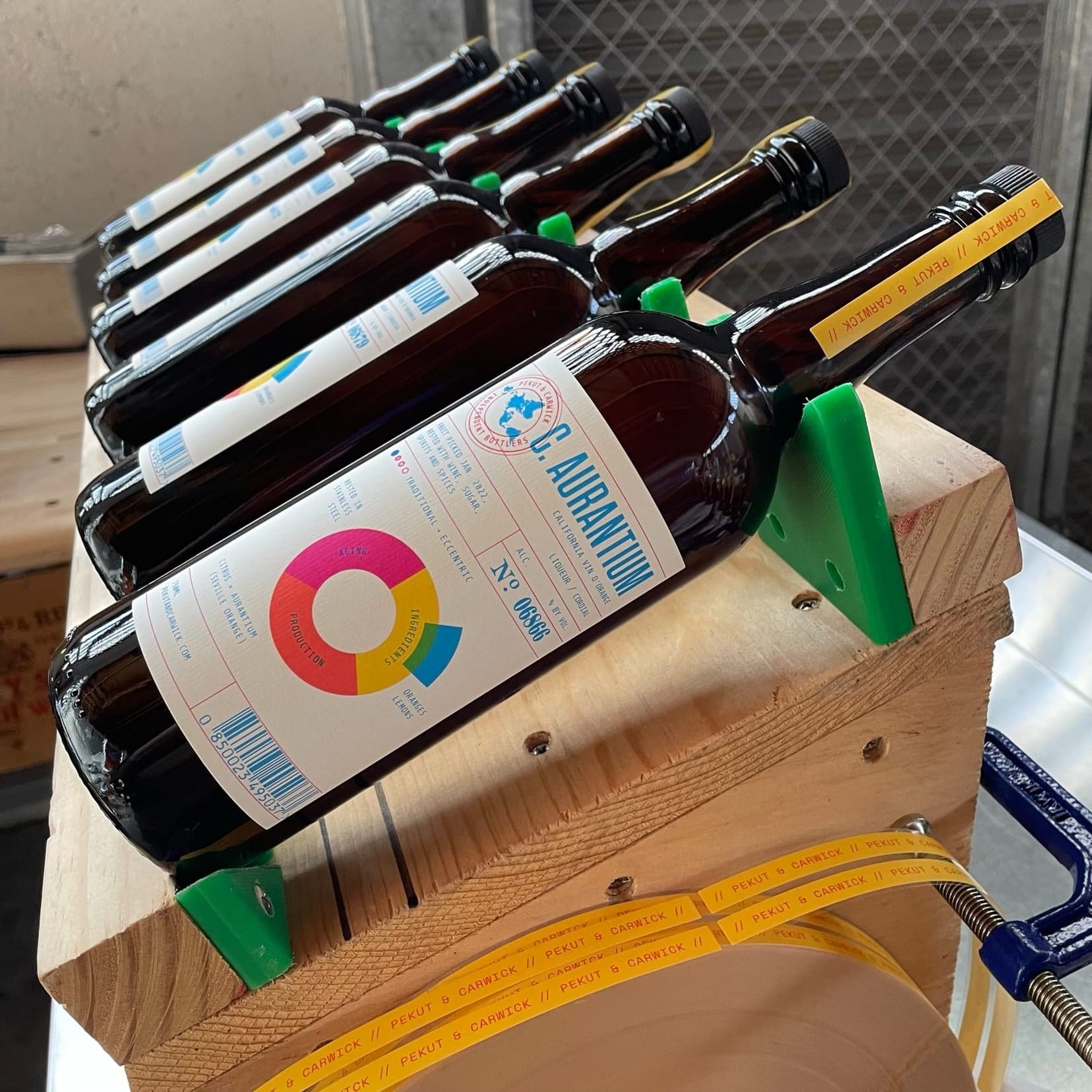 Six bottles of Pekut and Carwick Independent Bottlers Citrus Aurantium Vin D'Orange lined up on a wooden labeling jig.