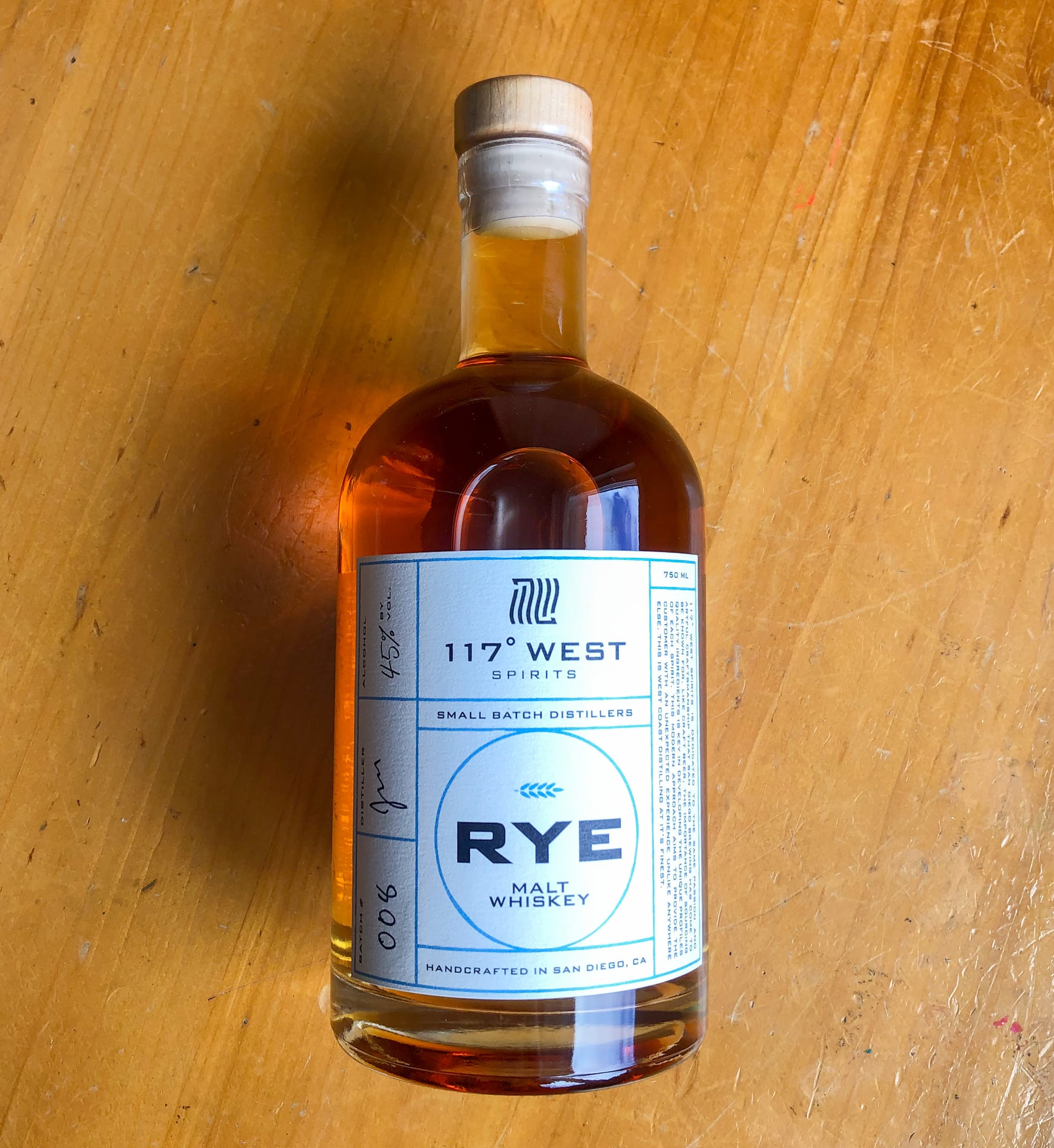 A bottle of 117° West’s Rye Malt whiskey lies atop a wooden table.